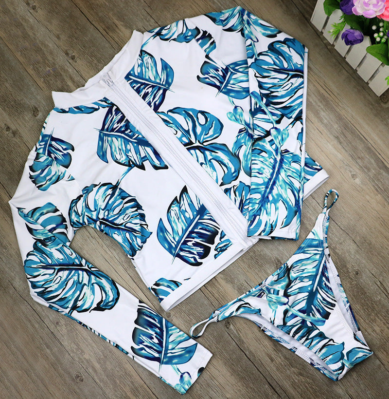 Women’s one-piece swimsuit laid flat with teal leaf print, long sleeves, white zipper